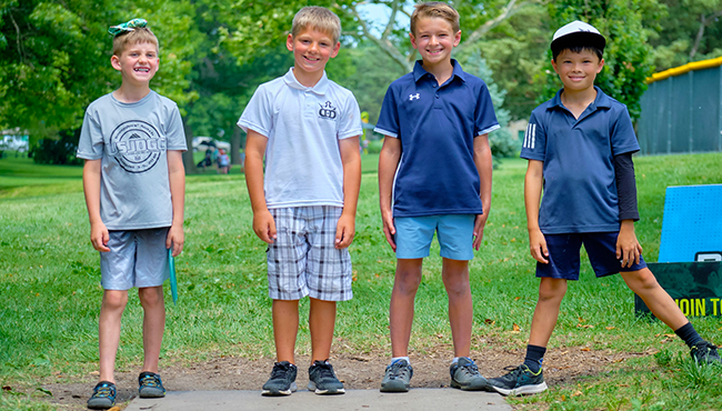 4 children, smiling and posing for a picture before teeing off